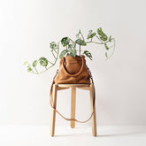 status anxiety last mountains leather handbag in tan with plant growing out of it