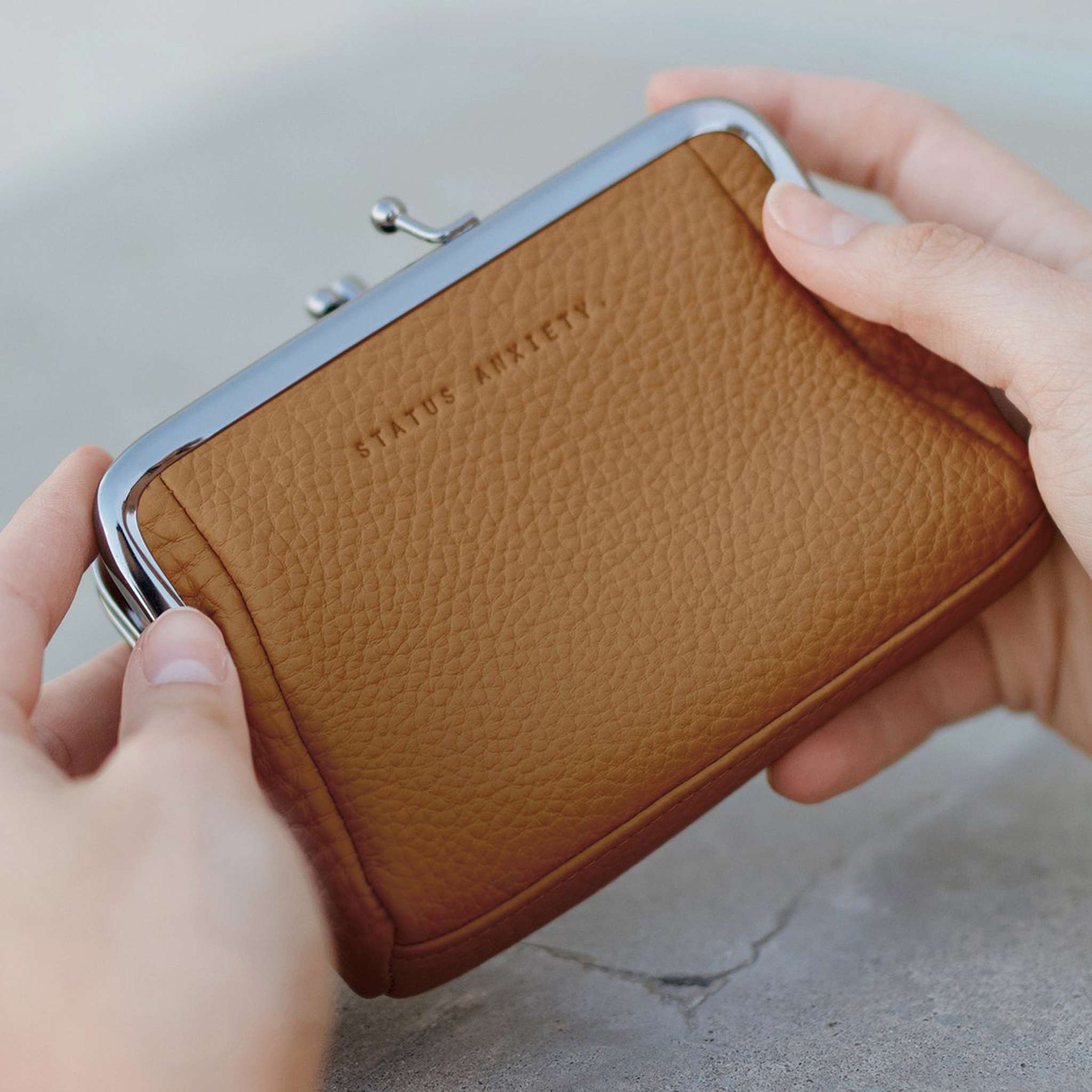 woman holding status anxiety volatile wallet purse in tan